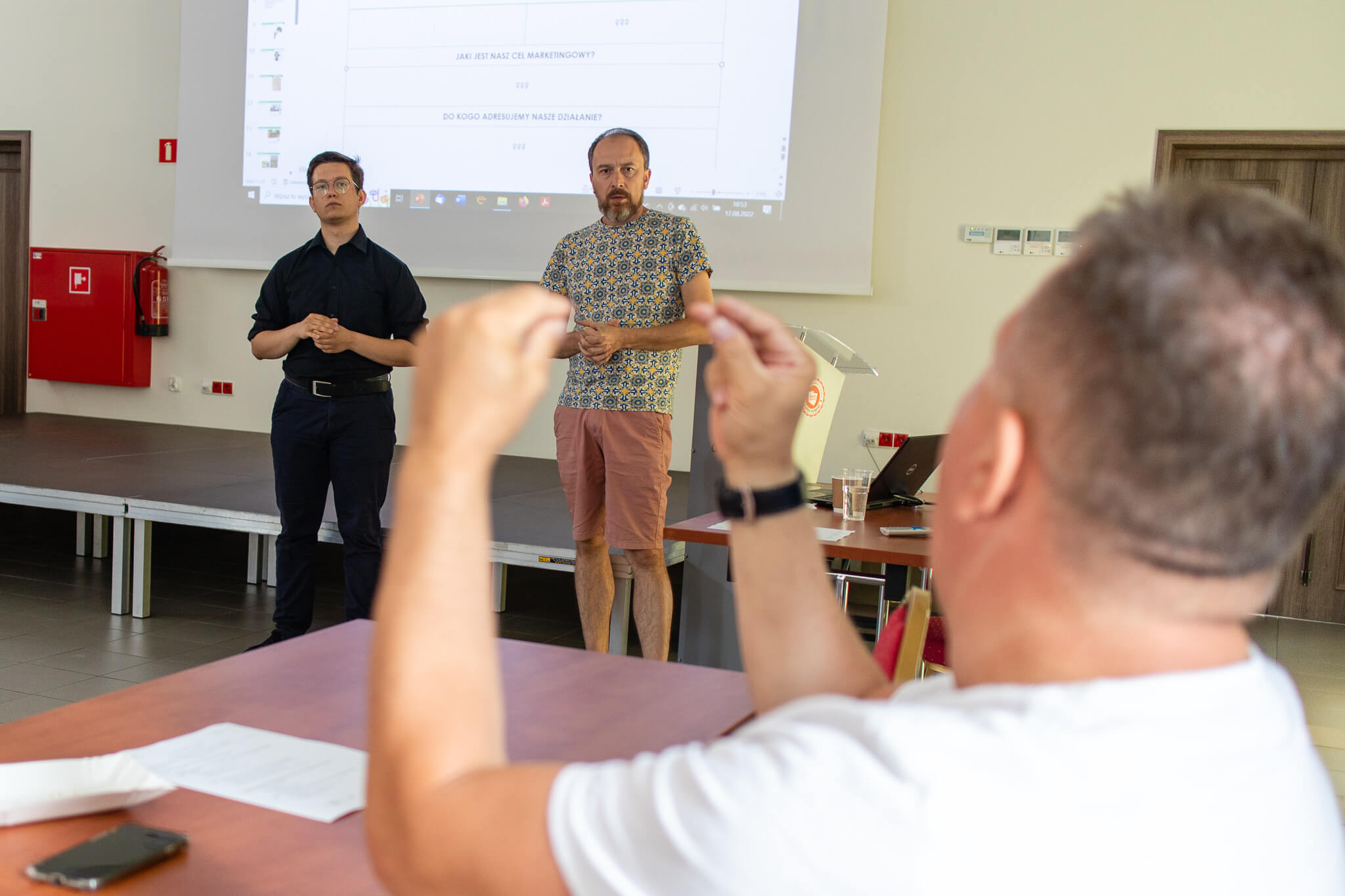 Głuchy mężczyzna rozmawia z osobą prowadzącą szkolenie, obok niego stoi tłumacz języka migowego