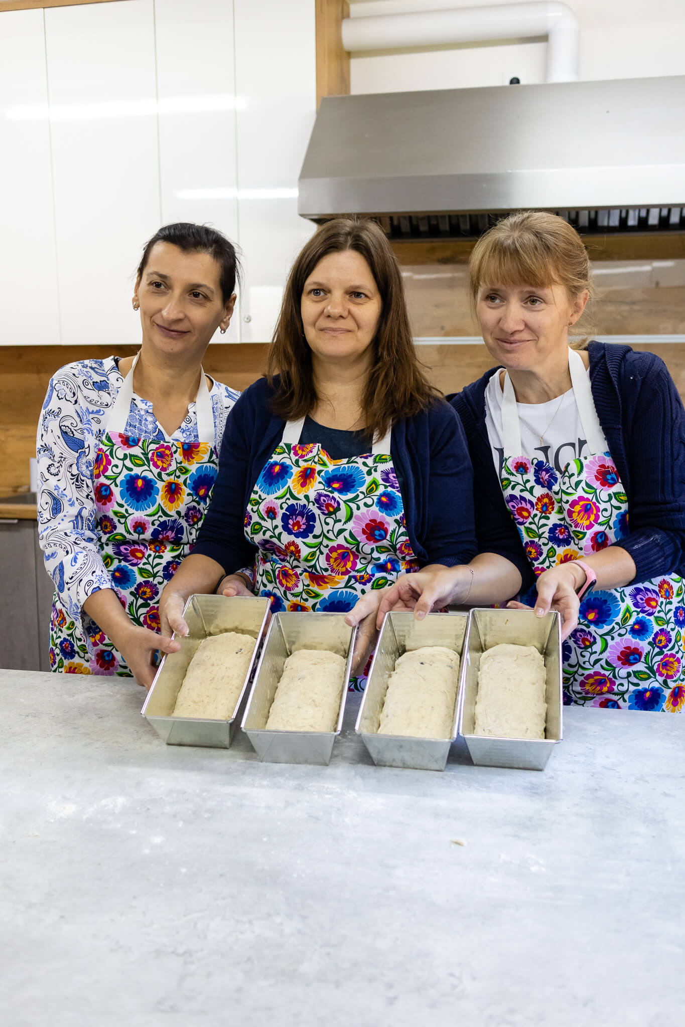 3 kobiety pozujące do zdjęcia z 4 blaszkami z ciastem na chleb