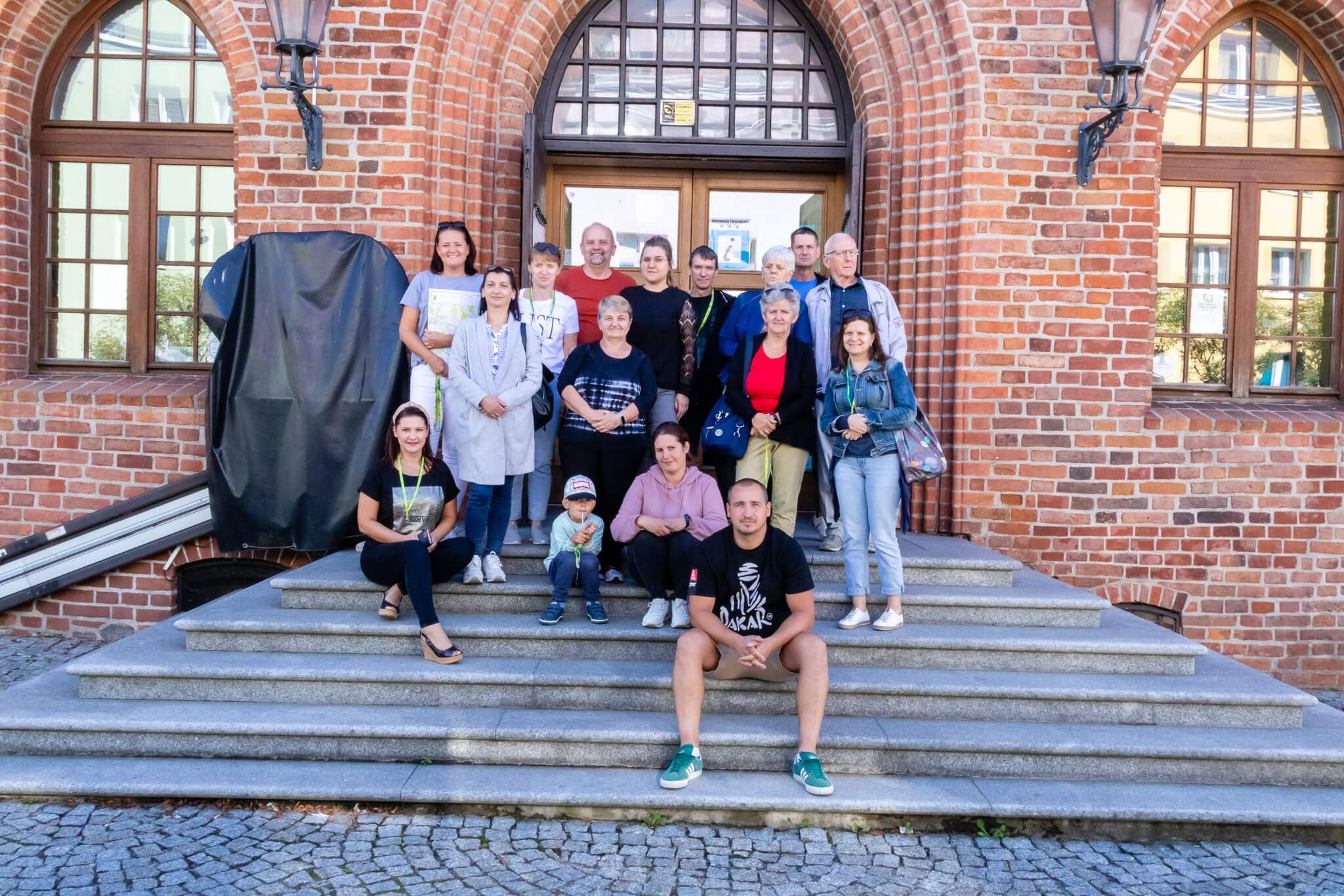 Grupowe zdjęcie członków stowarzyszenia stojących na schodach przed ratuszem w Morągu