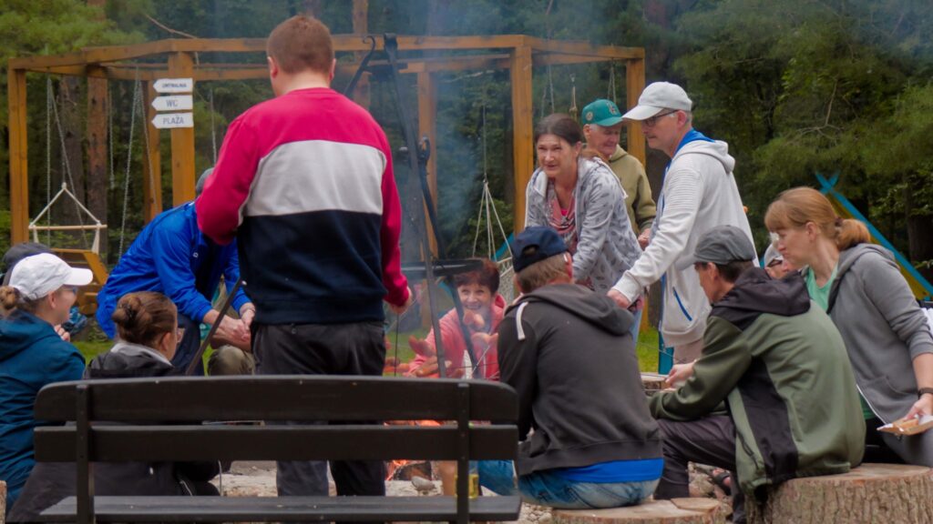 10 Grupa niesłyszących rozmawia, śmieje się i piecze kiełbaski nad ogniskiem.