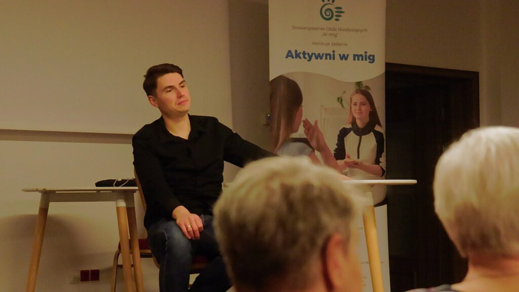 Bloger Filip Gałązka siedzi i słucha uczestników spotkania